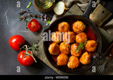 Homemade Meatballs with spices and tomato sauce in a frying pan on dark stone table. Flat lay, top view background. Stock Photo