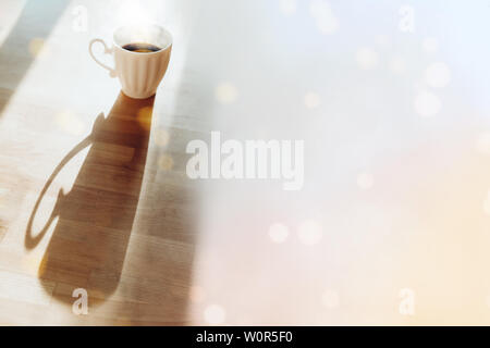 White cup with espresso standing on wooden table with long shadow side view. Breakfast tea with bokeh lights image. Good morning concept. Mug with hot Stock Photo