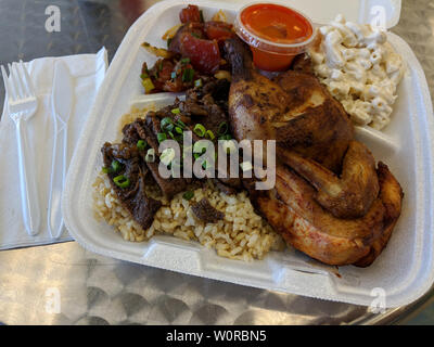 HFK Mixed Plate - Chicken, Beef, Poke with Rice and Mac Salad plus hot sauce on table with plastic fork and knife on napkin. Stock Photo
