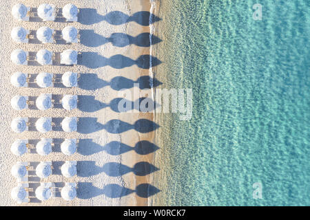 View from above, stunning aerial view of an amazing empty white beach with white beach umbrellas and turquoise clear water during sunset.