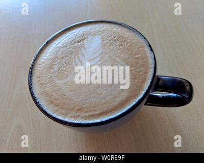Balck cup of Cappuccino on saucer with a leaf pattern in foam on table. Stock Photo