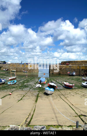 Frontal view of the harbour of Mousehole in Cornwall (UK) with boats on the beach at low tide and under a sunny summer sky with some clouds. Stock Photo