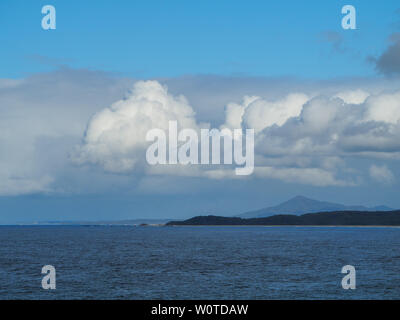 Beautiful day, Fluffy white Cumulus clouds set against the blue sky above the blue Pacific ocean, headland jutting out into the calm sea, Australia Stock Photo