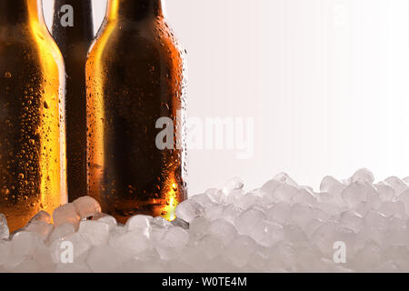 Three full beer bottles on crushed ice and white background close up . Horizontal composition. Front view. Stock Photo