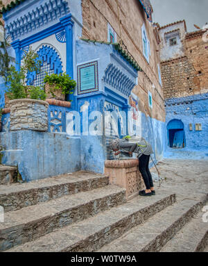 Chefchaouen, Morocco - May 4, 2019: A woman drinks water in one of the public fountains that can be found in the streets of the beautiful city of Chef Stock Photo