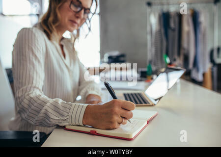 Female entrepreneur writing in her diary with laptop on desk. Online business owner working at her desk. Stock Photo