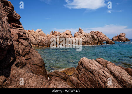 Red rock formation at a beach at Costa Paradiso in Sardinia (Italy) with turquoise and emerald green sea Stock Photo