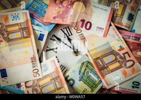 Euro currency and a clock, the hands stand five minutes before twelve. Stock Photo