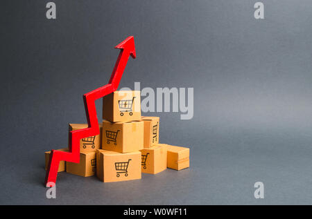 A pile of cardboard boxes with drawing of shopping carts and a red up arrow. The growth rate of production of goods and products, increasing economic Stock Photo