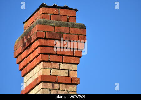 Vintage chimney of red bricks and mortar with corrugated sheet metal cover indicating it is not being used. Stock Photo