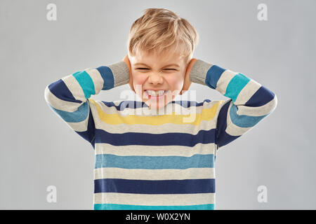 stressed boy in pullover closing ears by hands Stock Photo