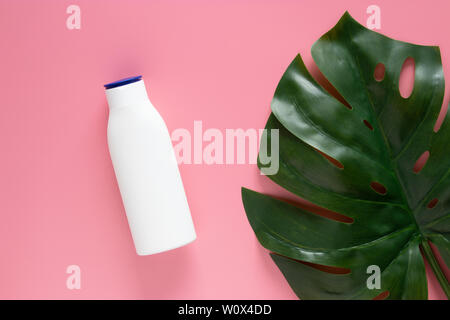 cosmetic nature skincare concept. white cosmetic bottle container with blank label for branding mock up, decorate with green tropical leaves on pink b Stock Photo
