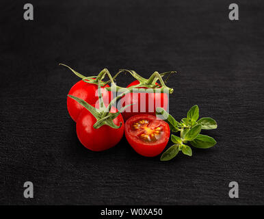 Red cherry tomatoes with green branch on black background Stock Photo