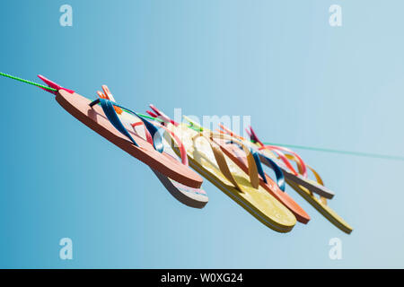 closeup of some different pairs of colorful flip-flops hanging on a clothes line against the blue sky, with a sunbeam Stock Photo