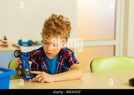 Constructed vehicle. Nice serious boy holding a constructor car while sitting in the classroom Stock Photo