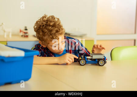Does it move. Serious cute boy touching a car model while wanting to move it Stock Photo
