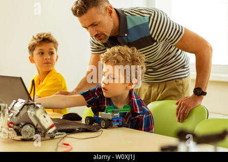 Computer class. Smart cute boy sitting in front of the laptop while working on it Stock Photo