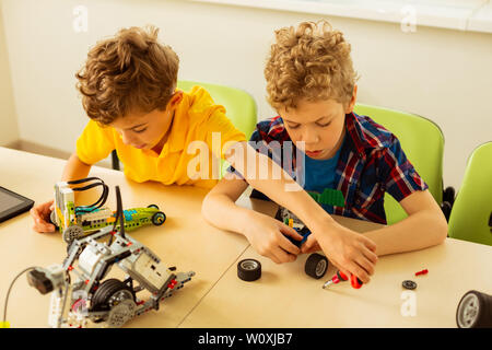 During engineering class. Top view of smart nice boys looking at the small details while constructing toys during their engineering class Stock Photo