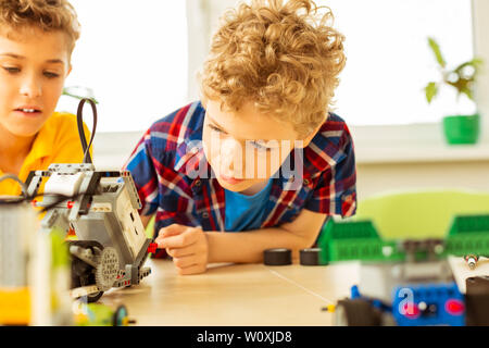 Modern robotics. Nice pleasant boy looking at the robot while being curious how it works Stock Photo