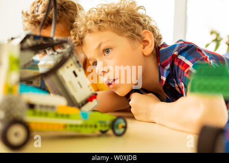Interesting science. Smart excited boy looking at the robot while being curious about robotics Stock Photo