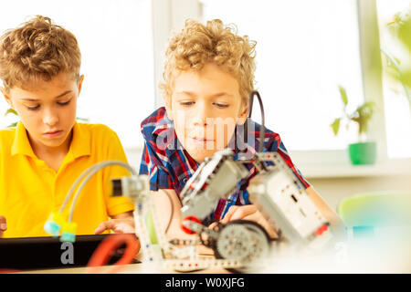 Lesson on robotics. Nice intelligent boys looking at the robot while having a science class on robotics Stock Photo