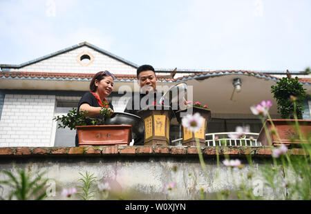 (190628) -- CHONGQING, June 28, 2019 (Xinhua) -- Liu Yi (R) and his wife Lu Kai water flowers at the courtyard of their home in Nanchuan District, southwest China's Chongqing, June 27, 2019. Despite losing his right arm in an accident at the age of nine, 44-year-old Liu Yi has never lowered his head towards destiny. After graduation from a vocational school in 1994, he tried a good many jobs like dishwasher, fruit dealer and coal miner. Since 2010, he has decided to start up his own business at his hometown by organizing villagers to plant bamboo roots and raising chickens. His efforts paid of Stock Photo