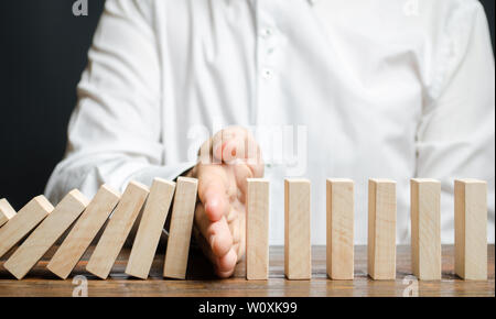 Businessman stops domino falling. Risk management concept. Successful strong business and problem solving. Reliable leader. Stop the destructive proce Stock Photo