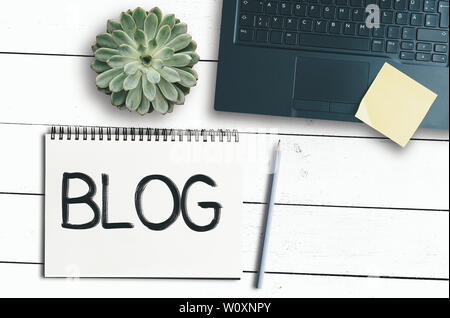 top view of word BLOG on spiral notepad on rustic white desk with laptop computer and potted plant Stock Photo