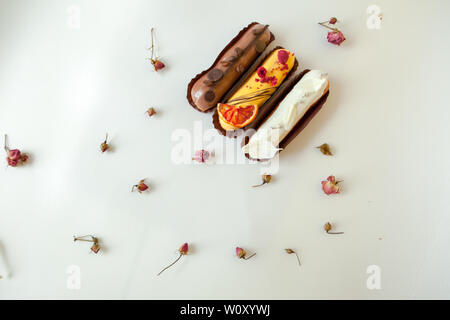 Set of three eclairs with different fillings and design. Isolate on a white surface decorated with dry roses, copyspace Stock Photo