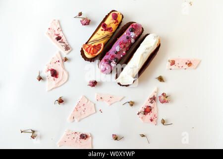 A set of three eclairs with different fillings and a design isolate on a white surface decorated with dry roses and white chocolate chips, copyspace Stock Photo
