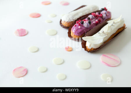 A set of three eclairs with different fillings and design isolate on a white surface decorated with drops of white chocolate, copyspace Stock Photo