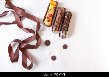 A set of three eclairs with different fillings and design isolate on a white surface decorated with chocolate drops and brown silk ribbon, copyspace Stock Photo