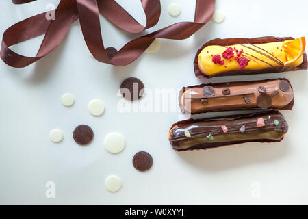 A set of three eclairs with different fillings and design isolate on a white surface decorated with chocolate drops and brown silk ribbon, copyspace Stock Photo