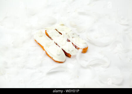 A set of three eclairs with white chocolate decor isolate on a white surface decorated with white feathers, copyspace Stock Photo
