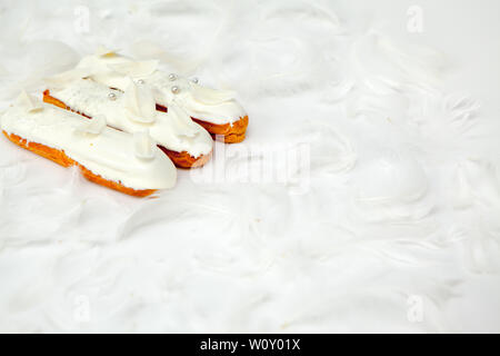 A set of three eclairs with white chocolate decor isolate on a white surface decorated with white feathers, copyspace Stock Photo