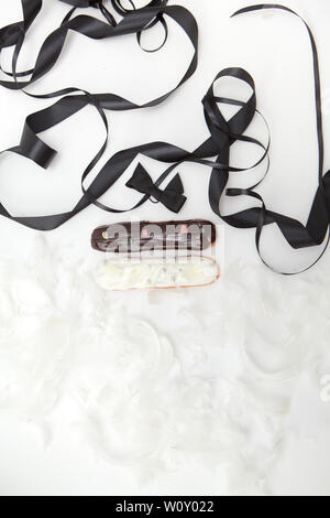 Set of two eclairs with a decor of black and white chocolate isolate on a white surface decorated with white feathers and brown ribbons, copyspace Stock Photo
