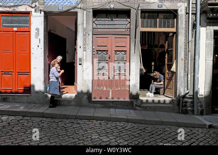 Porto neighbours two old women chatting on doorstep and young woman sitting by open door of shop in a street in Oporto Portugal Europe  KATHY DEWITT Stock Photo