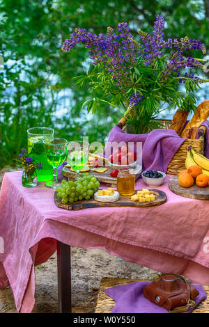 picnic near water at table with flowers in forest different kind of food fruits Stock Photo