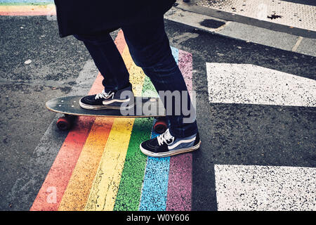 Person on a board wearing Vans shoes on the streets of Paris over a painted Pride Flag. Stock Photo
