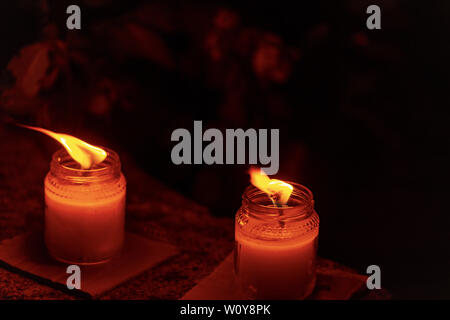 Two wax candles in glass jars with burning flame in the night, dark background Stock Photo