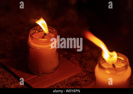 Two wax candles in glass jars with burning flame in the night, dark background Stock Photo