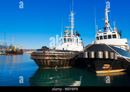 Two tugboats and containers ship docked in the harbor of La Spezia, Liguria, Italy Stock Photo