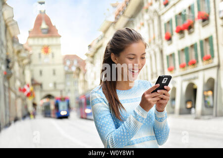Woman on smart phone walking on Kramgasse, Berne main street in the old city. Young female using smartphone app visiting tourist attractions and landmarks. Stock Photo