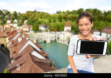 Smartphone screen - Woman showing app in Bern Switzerland, Europe. Girl holding blank empty smart phone screen on travel with copy space. Happy smiling Asian girl in Swiss Berne. Focus on screen Stock Photo