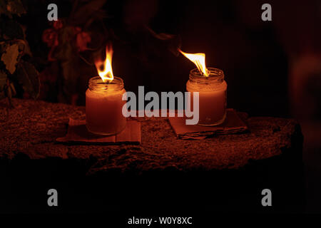 Two wax candles in glass jars with burning flame in the night, dark background Stock Photo