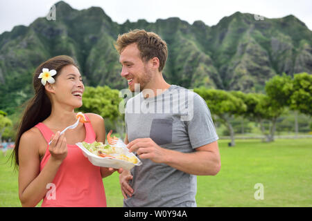 Hawaii food travel couple eating garlic shrimps on Oahu's North Shore. Popular Hawaiian shrimp food truck meal on road trip concept. Stock Photo