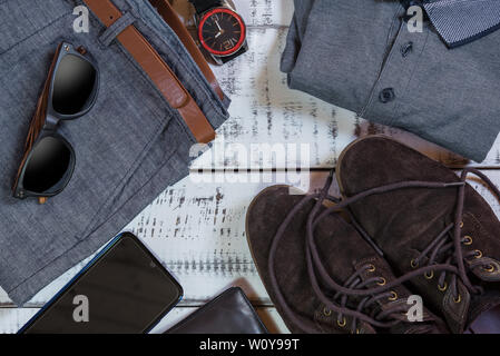 jean dress with brown belt,grey polo,brown shoes,sunglasses,watch,smartphone and wallet on a white wooden table Stock Photo