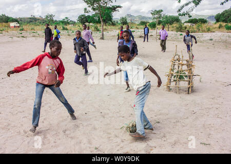 Children playing football barefoot with a handmade ball made with rags in a sandy field in rural Mozambique Stock Photo