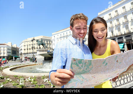 Tourists couple with map in Madrid. Sightseeing people looking at map for tourist attractions and famous landmarks while visiting Puerta del Sol in Madrid, Spain. Multiracial couple. Stock Photo