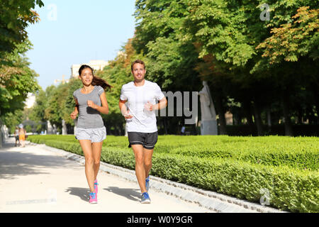 Running couple runners jogging in city park. Exercising woman and man runner training together on run living healthy active lifestyle in Buen Retiro Park, Parque el Retiro in Madrid, Spain, Europe. Stock Photo